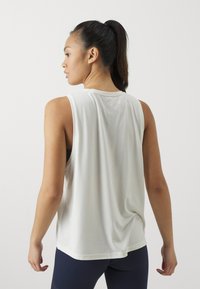Witte, mouwloze sporttop van lichtgewicht stof met een relaxte pasvorm, voorzien van een ronde hals en een gedrapeerde achterkant, gecombineerd met marineblauwe leggings.