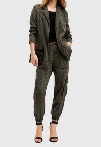 Olivgrön blazerväska med leopardmönster och cargobyxor med elastisk mudd. Modellen håller i en svart clutch och har på sig svarta klackar med remmar.