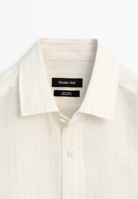 Weißes Leinenhemd mit Kragen, vorderen Knöpfen und schwarzen Etiketten mit der Aufschrift „Massimo Dutti“ und „100% Leinen Hergestellt in Ägypten.“