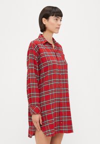 Abito camicia a quadri rossi realizzato in cotone. Presenta maniche lunghe, un'apertura frontale con bottoni, colletto e una vestibilità rilassata con spacchi laterali.