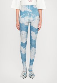 Leggings de denim con un estampado de nubes en azul claro y blanco, diseño de cintura alta, combinados con zapatos plateados acentuados con un lazo.