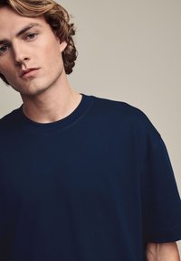 Camiseta de algodón azul marino con cuello redondo y mangas cortas, con una textura suave y un corte relajado, parcialmente visible en un modelo.