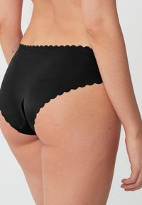 Zwarte high-waisted slips van gladde stof, met een scalloped tailleband en een naadloos ontwerp voor comfort. Zichtbare huidskleuren op de achtergrond.