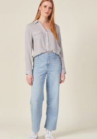 Jeans de tiro alto en azul claro con corte recto, combinados con una camisa de botones de patrón en gris y blanco. Zapatillas blancas.