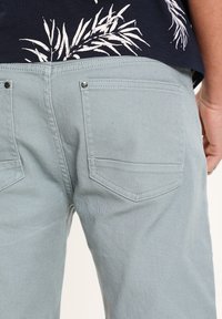 Pantalones de color azul claro con una tela texturizada, que presentan dos bolsillos traseros y botones de cromo, combinados con una camisa azul marino con patrones de hojas blancas.
