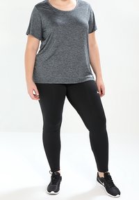 Camiseta atlética corta de manga gris combinada con legging negros y zapatillas negras, con un corte relajado y una textura suave.