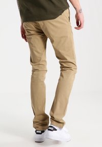 Khakibyxor i bomull med slim fit. Kombinerat med vita sneakers som har en svart logotyp på hälen. Minimalistisk design.