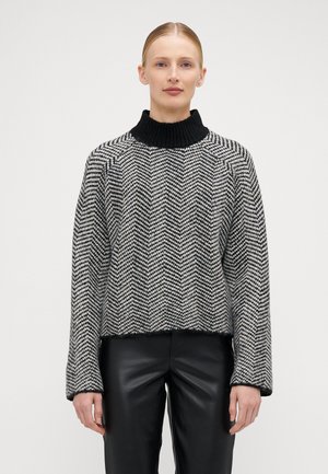 Pull en motif chevron noir et blanc avec un col roulé noir côtelé. Tissu texturé, design court et manches longues.