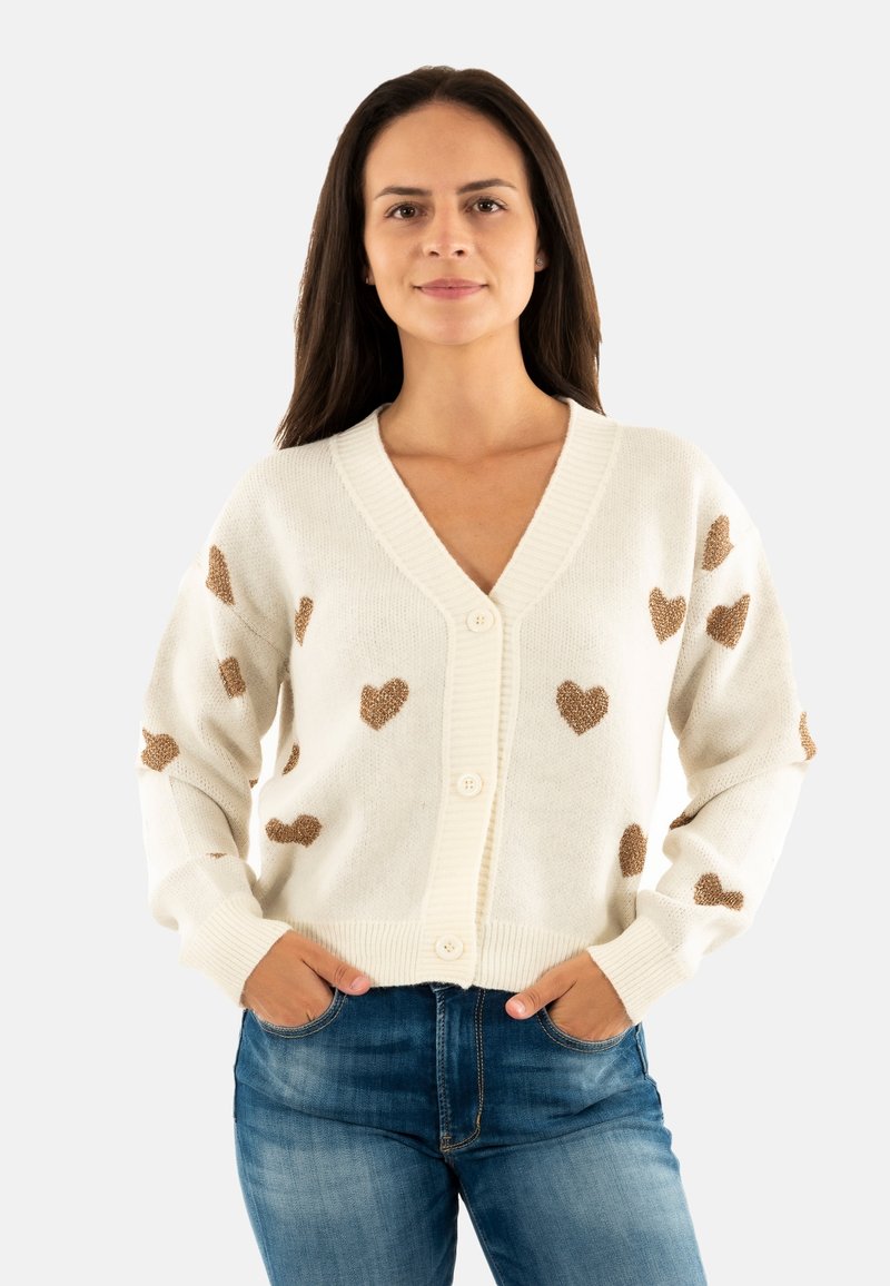 Cardigan lavorato a maglia crema con motivi a cuore bronzeo, scollo a V, chiusura con bottoni e polsini e orlo a coste, abbinato a jeans blu.