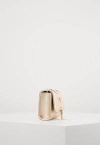 Borsa a mano metallic oro con superficie testurizzata e tracolla a catena. Presenta una chiusura con zip, una forma rettangolare e un piccolo ciondolo decorativo a frange.