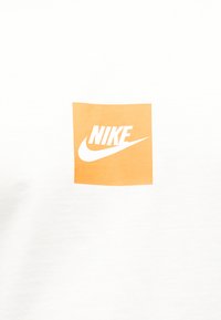 Λευκό ύφασμα με πορτοκαλί τετράγωνο στο κέντρο που φέρει το λευκό λογότυπο Nike και το σήμα swoosh στην επιφάνειά του.