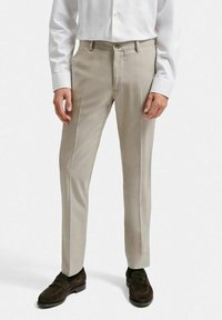 Beiga skräddarsydda byxor med en slät textur, med dragkedja och knappstängning. Bärs med en vit skjorta och bruna loafers.