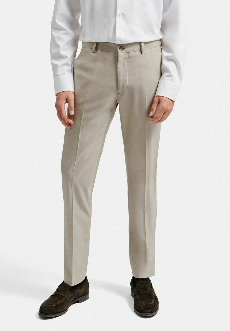 Beiga skräddarsydda byxor med en slät textur, med dragkedja och knappstängning. Bärs med en vit skjorta och bruna loafers.