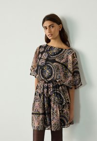 Losse zwarte jurk met paisley-patroon in roze, blauw en geel; korte mouwen, getailleerde taille en gelaagde zoom. Zachte stoftextuur.