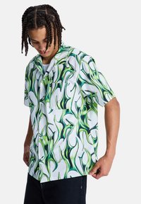 Πουκάμισο με κοντά μανίκια, λευκή βάση με πράσινα αφηρημένα μοτίβα. Κατασκευασμένο από υφασμένο ύφασμα, περιλαμβάνει τσέπη στο στήθος και κουμπιά μπροστά.