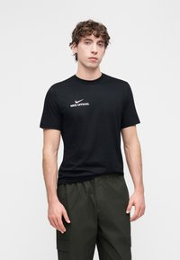 Crna pamučna majica kratkih rukava s bijelim Nike logotipom i tekstom "NIKE OFFICIAL" na prednjoj strani. Jednostavan dizajn s okruglim izrezom.