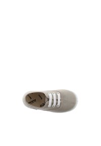 Zapato de lona beige claro con cordones blancos, puntera redonda y suela de goma. Presenta el logotipo de la marca en el interior y una etiqueta colorida en el costado.