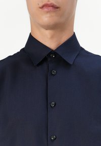 Camisa de botones azul marino con cuello clásico, tejido texturizado y botones negros a lo largo de la tapeta delantera.