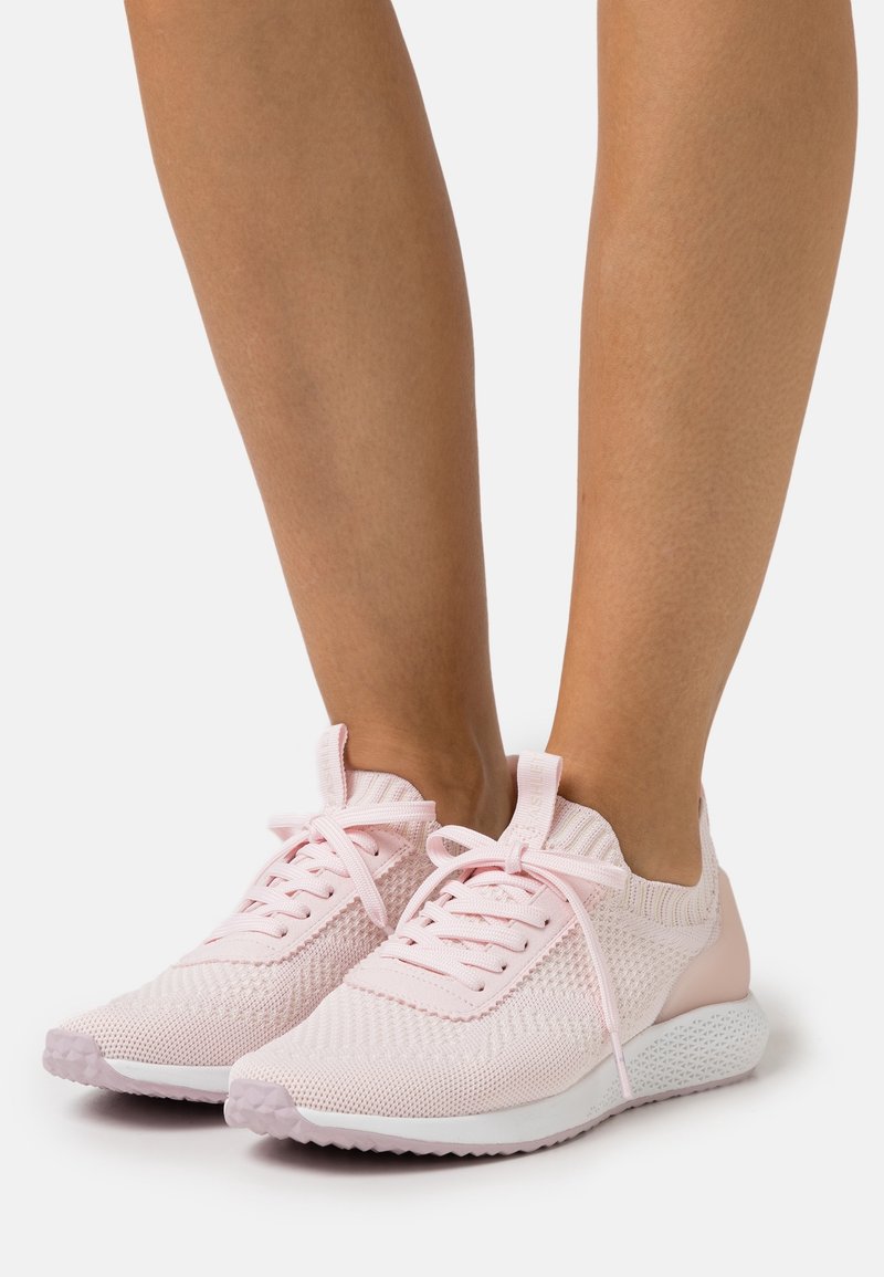 Světle růžové sneakers vyrobené z prodyšného síťového materiálu, s texturovaným designem, kulatými tkaničkami a polstrovanou bílou podrážkou.