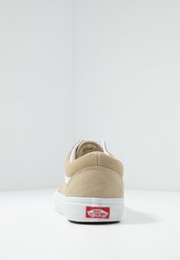 Sneaker in suede beige con dettagli bianchi e tacco arrotondato. Presenta una soletta in gomma bianca e un logo rosso "VANS OFF THE WALL" sul tallone.