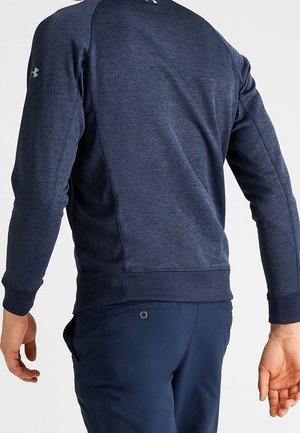 Mand iført navyblå langærmet sportstrøje og matchende bukser, set bagfra med afslappede arme.