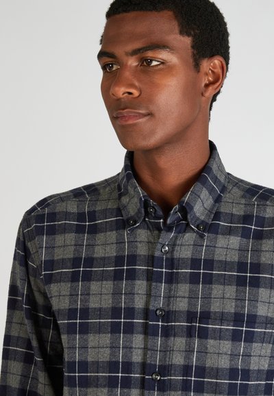 Camisa de cuadros en azul marino y gris, con cuello, que presenta un bolsillo frontal y botones negros, fabricada en una suave tela texturizada.