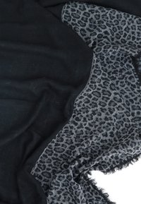 Sciarpa nera in morbido materiale testurizzato con motivo leopardato in sfumature di grigio. I bordi sono sfrangiati, valorizzando il design.