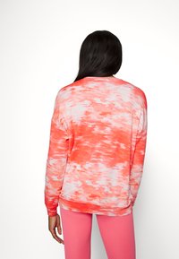 Pulôver de manga longa em padrão tie-dye nas cores coral e branco; textura suave e corte relaxado com decote canelado, combinado com leggings cor-de-rosa.