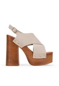 Sandalias de plataforma de ante beige con diseño de tira ancha, un tacón de bloque de madera alto y acentos de tachuelas en tono dorado.