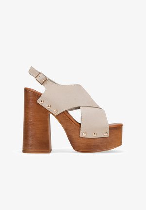 Sandalias de plataforma de ante beige con diseño de tira ancha, un tacón de bloque de madera alto y acentos de tachuelas en tono dorado.