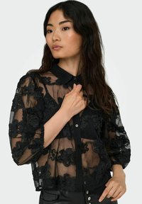 Must hakk blouse lille lillelille lillelillemustre, nööpidega esi ja krae. Pika puff-varrukad ja tekstuuriga kangas lisavad detaili.