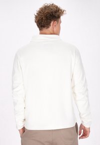 Witte langemouwen polo-shirt met een zachte textuur, een omgevouwen kraag en een rechte zoom, gedragen met lichtbruine broek.