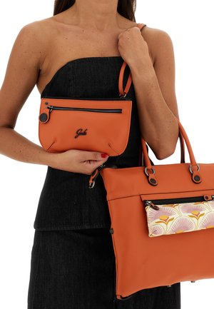 Due borse in pelle arancione tenute insieme. Una è una borsa più grande con una tasca frontale a motivo floreale, l'altra è una pochette più piccola con cerniera.