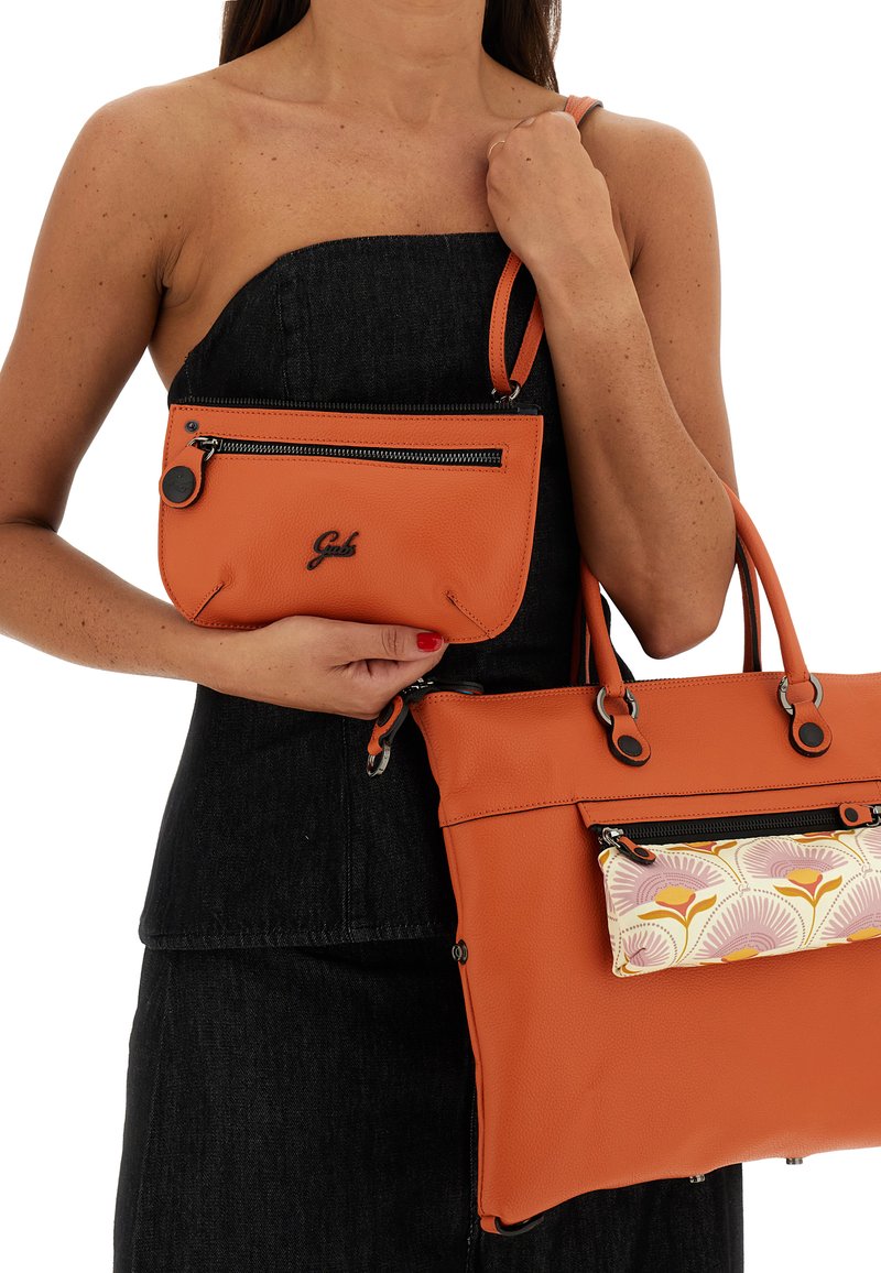 Due borse in pelle arancione tenute insieme. Una è una borsa più grande con una tasca frontale a motivo floreale, l'altra è una pochette più piccola con cerniera.