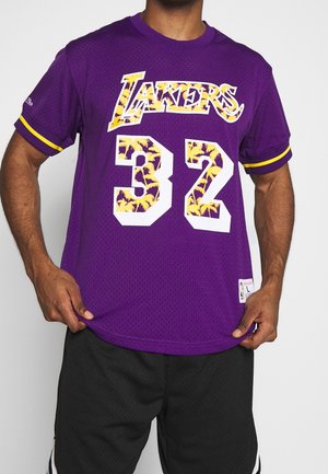 Osoba nosząca fioletową koszulkę Los Angeles Lakers z numerem 32 z żółtymi wzorami palmowymi na literach i cyfrach.