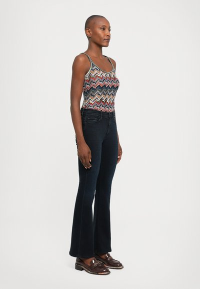 Multicolored zigzag-patterned tank top, dark blue flared jeans, and brown loafers. Smooth fabric with a fitted silhouette and structured design.