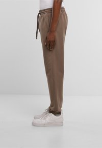 Tan joggerbroek met een elastische tailleband en trekkoord, voorzien van zijzakken en bijgesneden enkels, gecombineerd met witte sneakers.