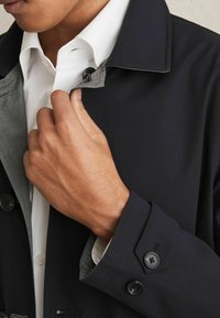 Palton negru cu interior gri, detalii cu nasturi și un design modern al gulerului. Are un material texturat și un croi ajustat.