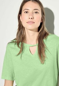 Grön kortärmad T-shirt med en subtil texturerad tyg och en nyckelhålsdetalj vid halsen. Regular fit med rundad nederkant.