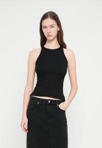 Μαύρο ριμπ τοπ χωρίς μανίκια με ψηλό λαιμό, εφαρμοστό σχέδιο και κοντό μήκος, συνδυασμένο με μαύρη φούστα από τζιν.