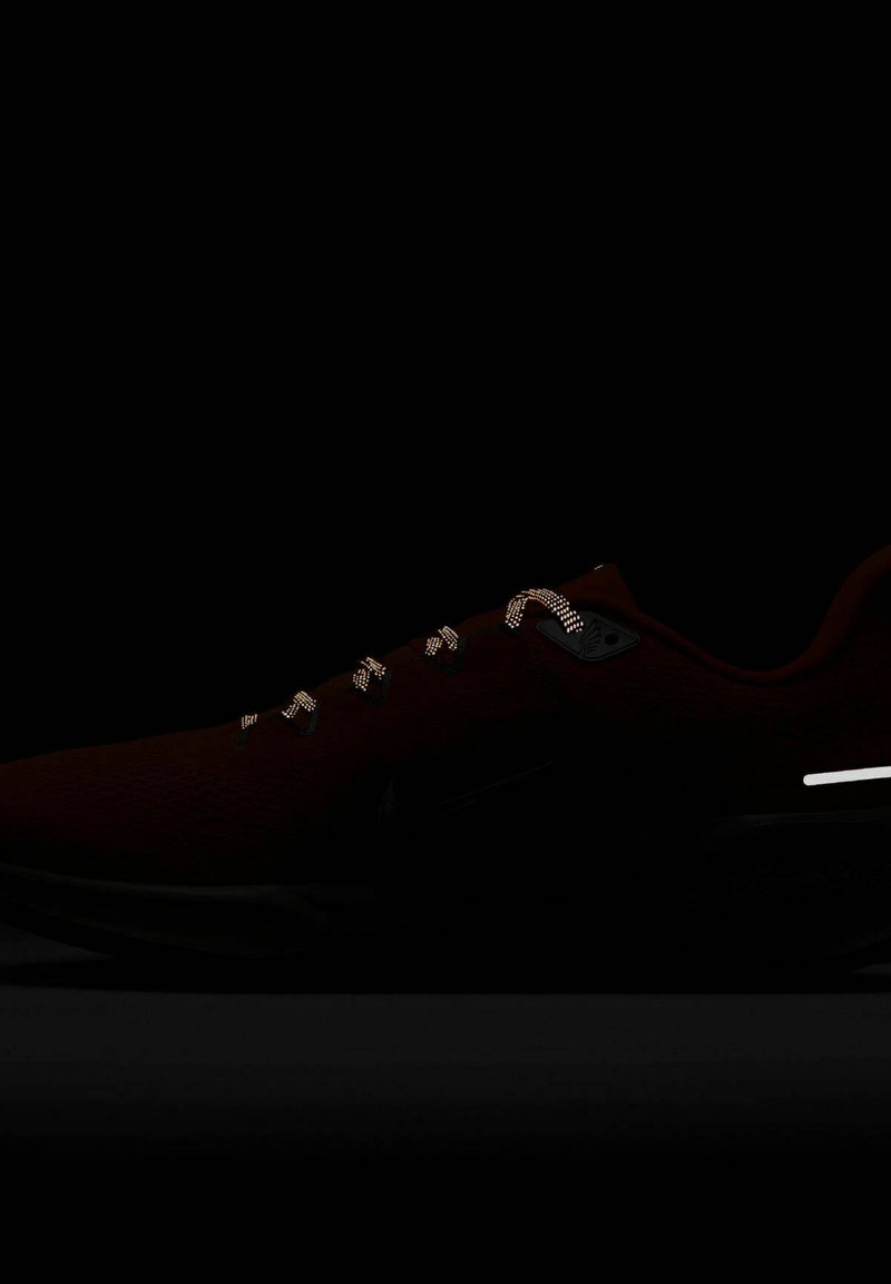 Chaussure de sport rouge avec une tige en mesh, accents noirs, détails réfléchissants et lacets à motifs. Design élégant avec une semelle rembourrée.