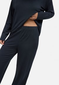 Conjunto de loungewear de corte relajado en azul marino oscuro. Parte superior de manga larga con dobladillo curvado, combinada con pantalones de cintura elástica. Tejido suave y liso.