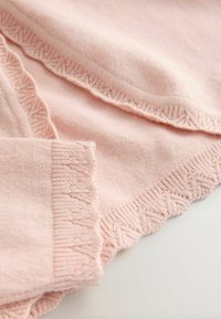 Jasnoróżowa dzianina z falbanką i wzorem z chevronu wzdłuż dołu i rękawów, podkreślająca miękką teksturę.