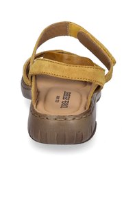 Sandale en suède jaune avec deux sangles réglables, semelle intérieure en tan rembourrée et semelle texturée marron. Design décontracté pour le confort et la stabilité.