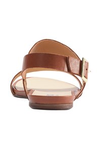 Sandal din piele maro cu talpă plată, având o curea reglabilă la gleznă și o cataramă aurie. Textură netedă, design cu vârf deschis.