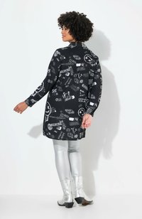 Túnica gráfica negra con estampados blancos, de mangas largas y corte recto, combinada con leggings plateados brillantes y botas metálicas hasta el tobillo.
