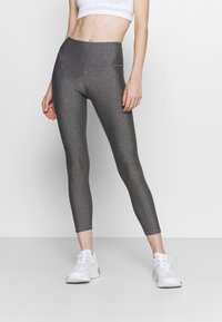 Grå, högmidjade leggings med en slät, texturerad yta, med en figurnära passform och ankellång fåll. I kombination med vita träningsskor.