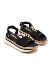 Sandali di stoffa nera con cinturini incrociati, una soletta in espadrillas intrecciata e una spessa piattaforma bianca. Suola in gomma marrone con grip testurizzato.