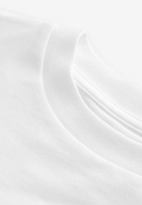 Détail d'un t-shirt en coton blanc présentant un col rond et un tissu doux et texturé, avec des coutures visibles le long du bord du col.