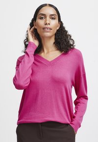 Rosa V-hals tröja med långa ärmar och avslappnad passform, gjord av mjukt tyg. Anmärkningsvärda detaljer inkluderar ribbade ärmslut och en jämn struktur.